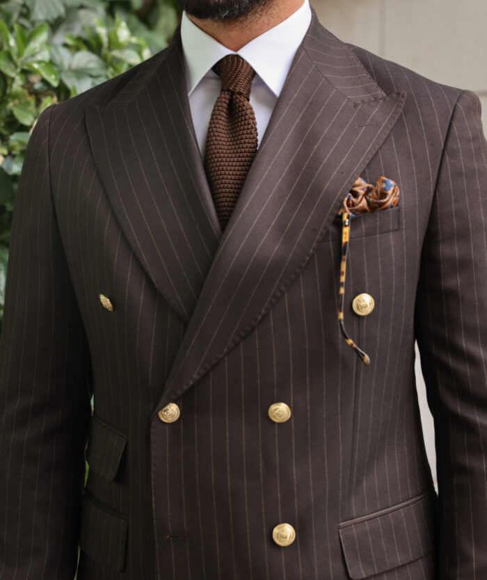 Tampers Close Slim fit dark brown double breasted two piece men's suit with peak lapels with decorative gold buttons.